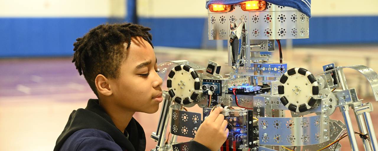 A boy works on a robot in a school classroom.